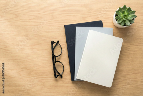 Top view of blank notebooks mockup stacked on  wooden desk with eyeglasses and succulent