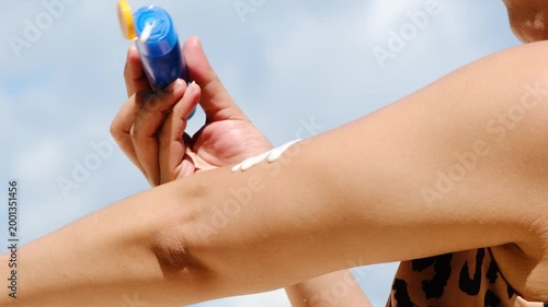 Sunscreen from blue bottle on palm she apply hand and arm with bright sun and blue sky background, skin protection and summer skincare concept