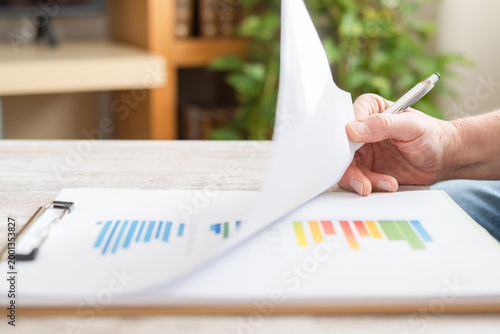 Photos Hand turning a business report page to reveal colorful bar charts and statistics