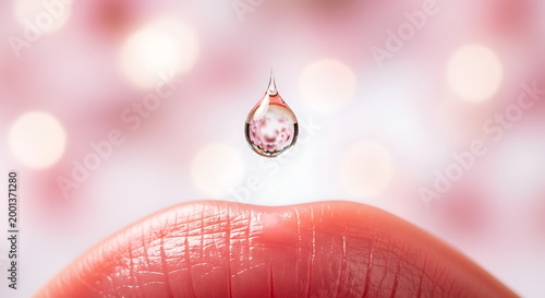 Delicate lip care essence droplet suspended above pink lip skin with blurred bokeh background