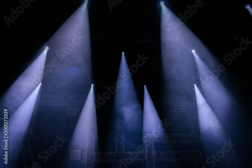 Stage lighting beams illuminate a dark venue with smoke effects, creating a dramatic atmosphere for a performance or concert setting