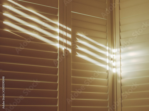Rays of sunlight coming through the slats of indoor window shutters