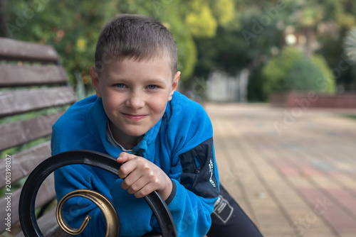 Portrait of a smiling cute nine-year-old boy. Child sitting on a park bench.