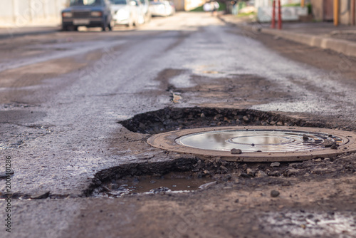 A pothole on an asphalt wet  road, showcasing the need for repair in the downtown area.