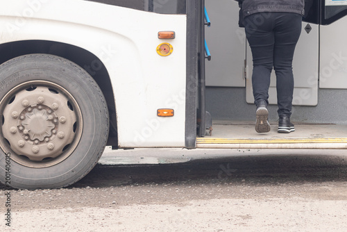Female passenger gets on the white coloured electric bus at a bus stop in city
