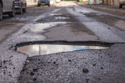 A large pothole filled with water in the middle of the road.