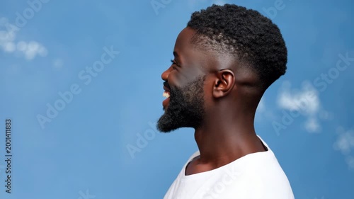 Male african young thoughtful portrait of a young adult man with beard and short haircut wearing a white t shirt against a soft blue backdrop looking contemplative and poised