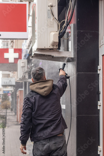 A technician cleans an outdoor air conditioner condenser unit with a pressure sprayer.