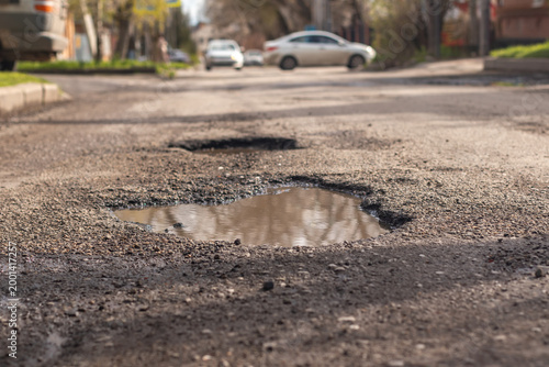 A pothole in the road and a car in the background that is moving towards this pothole
