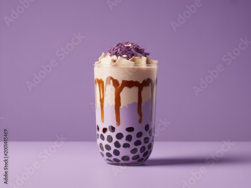 A glass of iced purple taro bubble tea topped with whipped cream and purple shavings, featuring dark tapioca pearls and caramel drizzle, purple background