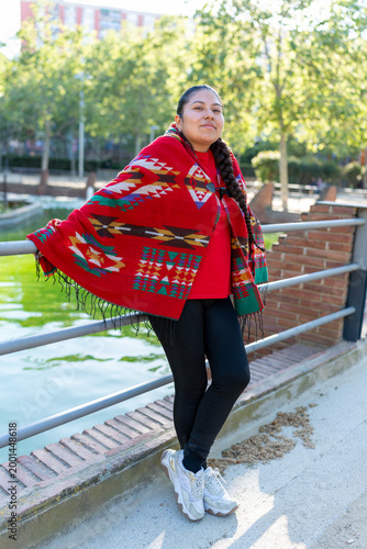 Latin woman posing outdoors, wearing a colorful poncho and traditional braid
