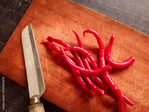 Fresh red chili peppers on a wooden cutting board with a knife for cooking preparation