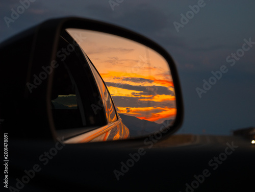 Cuadro en lienzo A stunning sunset lights up the mountains in the distance, beautifully mirrored in the side view mirror of a car on an evening drive