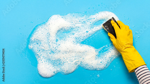 Φωτογραφία Person in a bright yellow rubber glove vigorously scrubs a blue surface with a black sponge