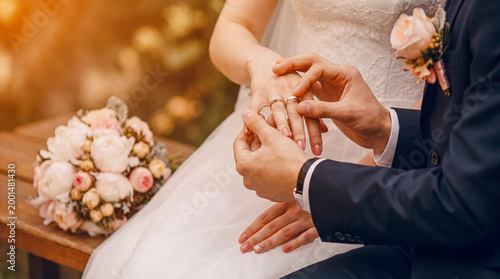 Tableau sur toile Groom placing wedding ring on bride's finger during an outdoor ceremony, with a bridal bouquet nearby