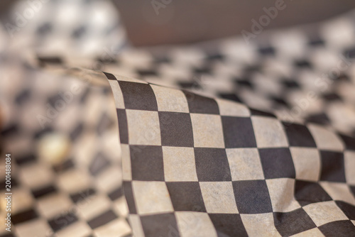 Black and white checkered paper covers food items. Paper wraps food, creating a checkered pattern. Folds and creases show soft, flexible texture. Grainy surface highlights material's natural feel