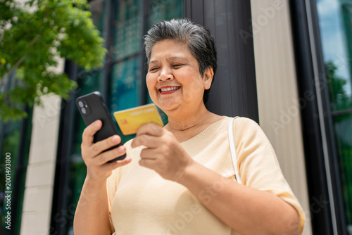 Asian senior woman using phone shopping online outdoors in the city. 