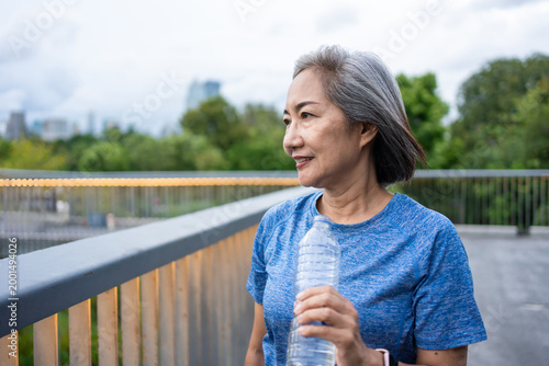 Asian senior woman drinking water while running exercise in the garden. 