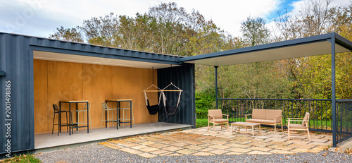 Banner of sustainable and modern shipping container lounge cafe outdoor, featuring an inviting outdoor terrace with hammocks arrangements, a covered patio, and a natural green lawn area
