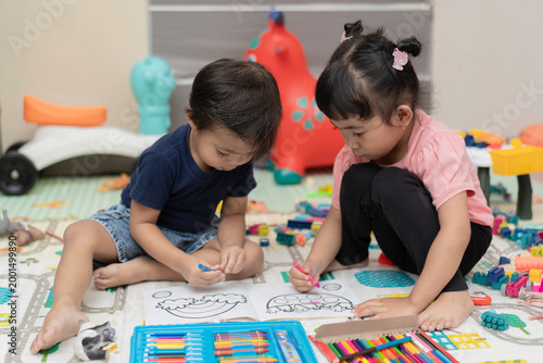 Two young children sitting on floor coloring book with crayons