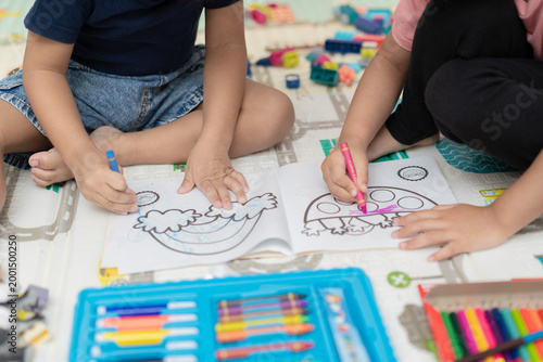 Close up of children's hands coloring a rainbow in a drawing book.
