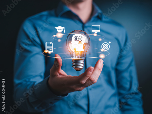 A man in a blue shirt holds a glowing lightbulb with educational icons floating around it