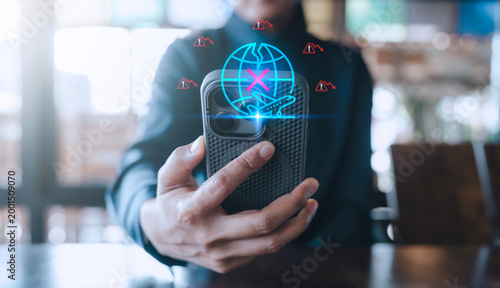 Obraz na płótnie Travel and tourism crisis concept depicted by a hand holding a smartphone with a glowing cancelled flight and cracked globe hologram amidst falling warning signs