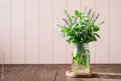 Fresh kitchen herbs and white flowers in a mason jar on a rustic wooden background