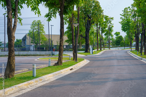 Empty asphalt road with green trees and parking lot on clear day, creating calm and peaceful outdoor environment