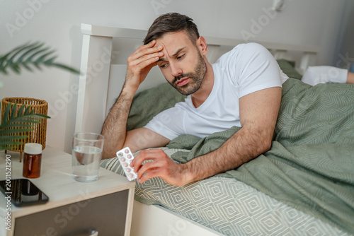 Foto Man suffering from headache and holding pills in bed