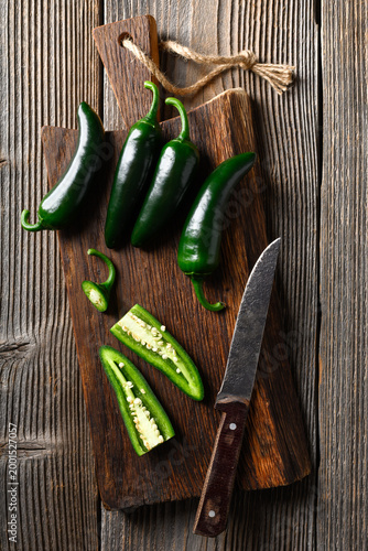 Black jalapeno with knife on rustic wooden cutting board close up. Green mexican jalapeno hot peppers
