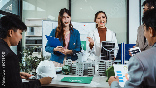Business team meeting with engineers discussing renewable energy project using solar panel and wind turbine models in modern office, presenting green city planning concept