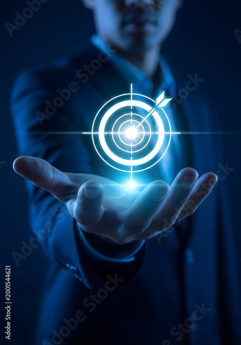 Businessman holding a glowing target icon with an arrow hitting the bullseye, representing business goals, success, marketing strategy, and focus