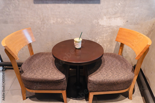 Top View of Modern Cafe Seating Area with Wooden Chairs and Iced Matcha Latte on Round Table Against Concrete Wall