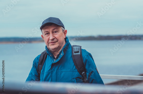 Smiling Senior Man in Blue Jacket and Cap by Riverside. Approachability and Well-being Concept