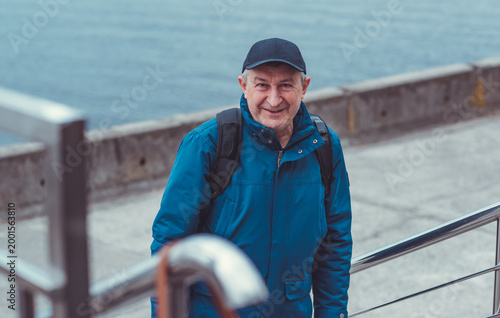 Smiling Senior Man in Blue Jacket and Cap by Riverside. Approachability and Well-being Concept