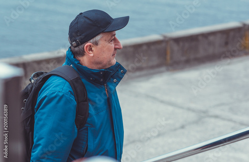 Smiling Senior Man in Blue Jacket and Cap by Riverside. Approachability and Well-being Concept