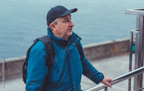 Smiling Senior Man in Blue Jacket and Cap by Riverside. Approachability and Well-being Concept