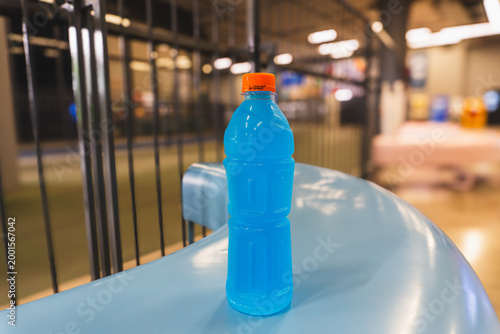 Iced Blue Isotonic Sports Drink in Unlabeled Plastic Bottle with Orange Cap on Blue Surface in Gym Setting