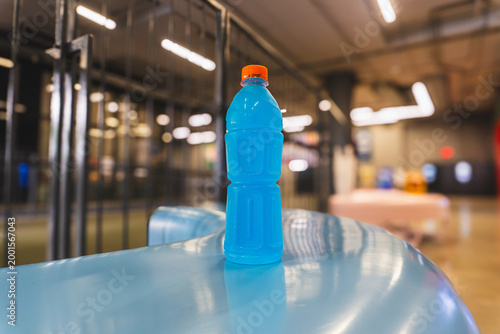 Blue Isotonic Sports Drink in Unlabeled Plastic Bottle with Orange Cap on Blue Surface in Modern Urban Fitness Center