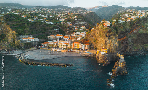 Photos An aerial shot captures the coastal village of Ponta do Sol in Madeira, featuring colorful buildings nestled between steep cliffs and a pebble beach by the Atlantic Ocean