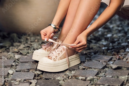 A man ties his shoes on a platform. The shoes are on the cobblestones. The hands are carefully tied with ribbons.