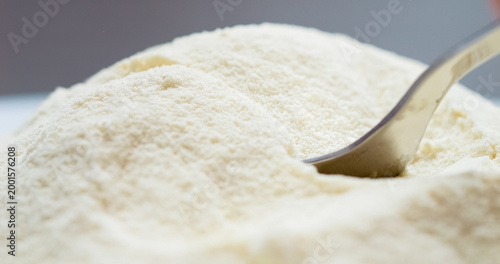 A spoon is filled with fine powdered milk as it pours smoothly. The texture and color of the milk powder are highlighted in this intimate view.