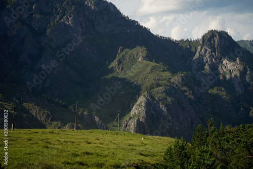 фотографія Power transmission towers crossing a green forest against a backdrop of mountains and blue sky