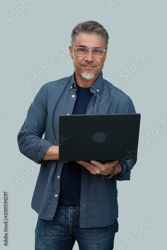 Casual mid adult man standing holding laptop computer. Portrait of happy middle aged male in 50s with gray hair and glasses, smiling. Isolated on white background.