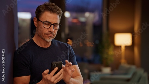 Portrait of happy middle aged man at home at night in dark, cosy living room. Serious mid adult man concentrating. .