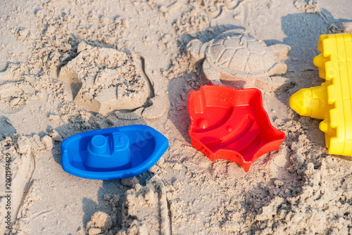 Beach Toys on Sandy Canvas: Colorful beach toys, sculpted in a variety of fun shapes, rest on a sun-kissed expanse of beach sand, telling stories of seaside summer fun.