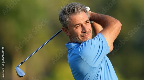 Senior amateur golf player on course hitting the ball, swinging the club, smiling. Portrait of middle aged, older man enjoying leisure activity. Health, sport and lifestyle .