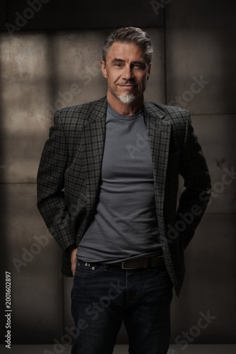 Casual mid adult man standing. Portrait of happy middle aged male entrepreneur in 50s with gray hair, smiling. Confident businessman in business casual on gray background.