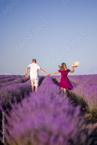 A young couple runs in a lavender field. View from the back, hat in hand. Feeling of freedom and joy